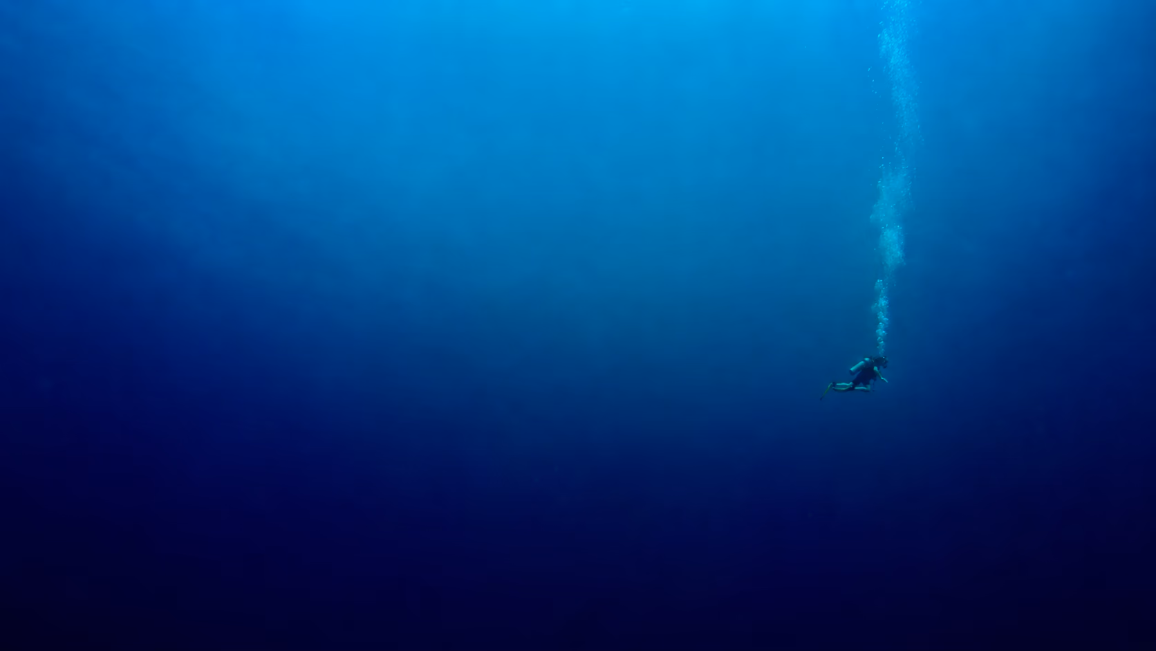 Taucherin im tiefblauen Wasser, über ihr eine Spur aus Luftblasen
